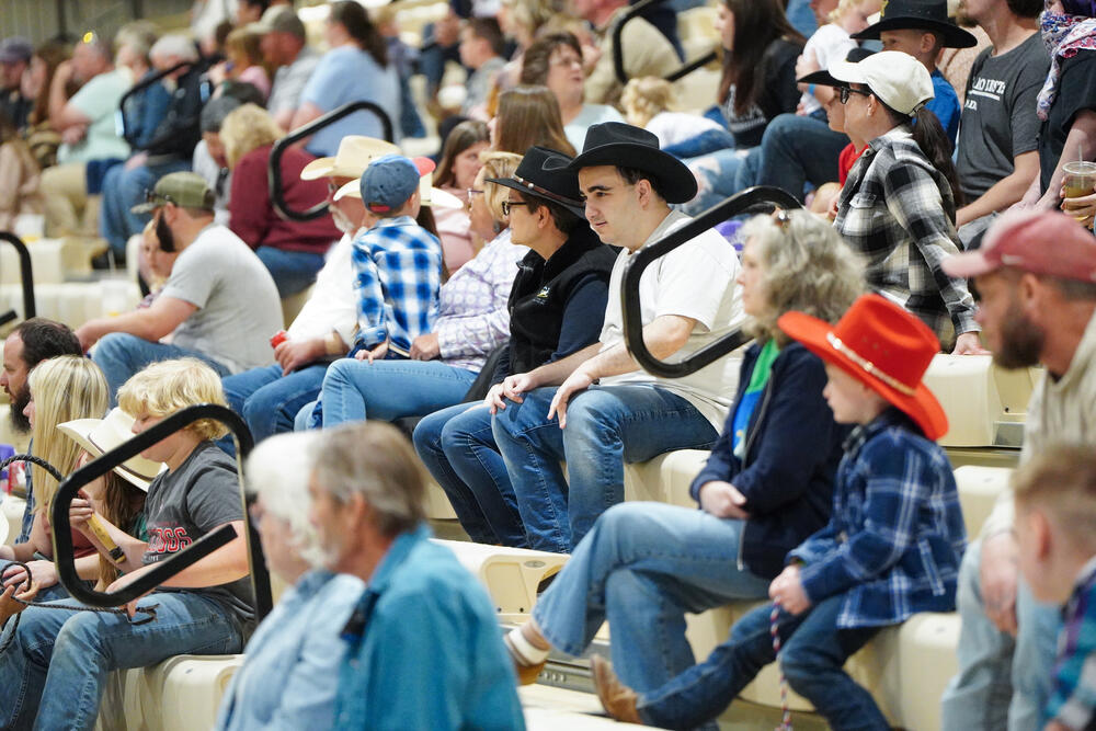 Rodeo patrons dressed in western attire sitting in bleachers watching the rodeo.