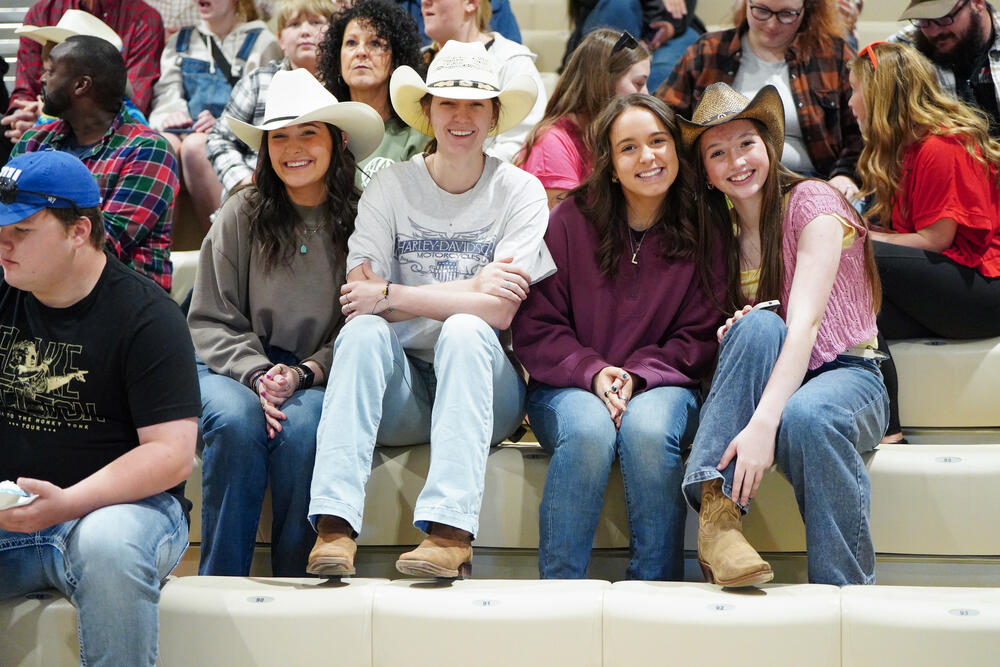 4 teenage girls wearing cowboy hats posing for the camera while sitting in the bleachers.