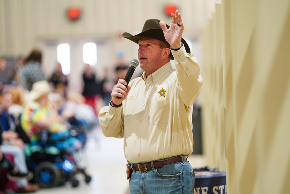 Sheriff Mark Moon greeting attendees of the special needs rodeo using a microphone.
