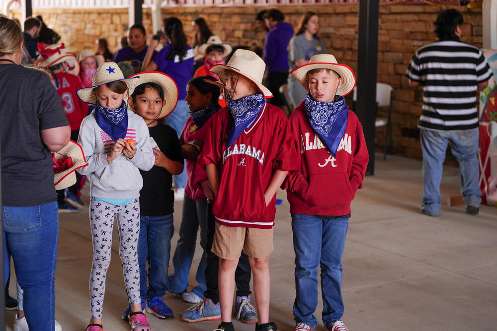 A group of young males wearning cowboy hats and bandanas waiting to play games. 
