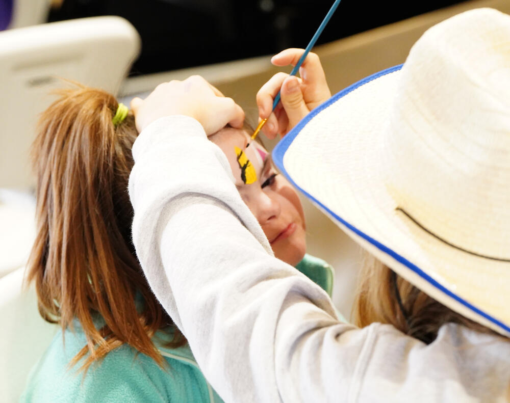A young female getting her face painted by a volunteer. 