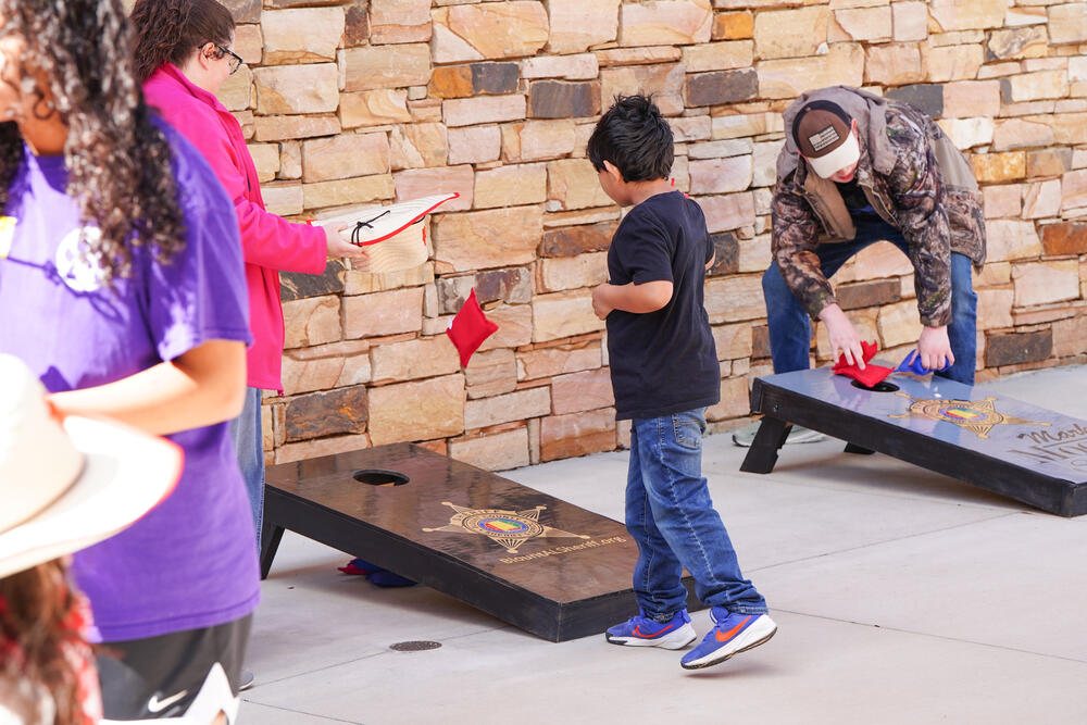 A young boy tossing a bean bag onto a cornhole board. 