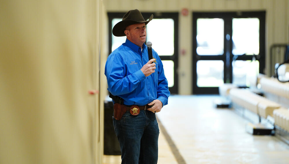 Sheriff Mark Moon wearing a black cowboy hat and blue shirt speaking into a microphone.